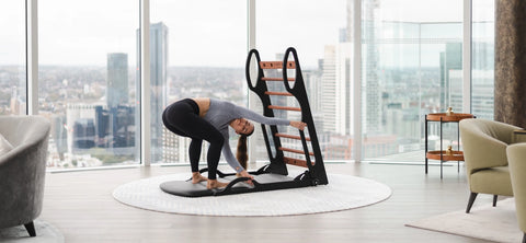 A woman in a yoga pose using a NOHRD Elasko, set in a modern living room with a city view.