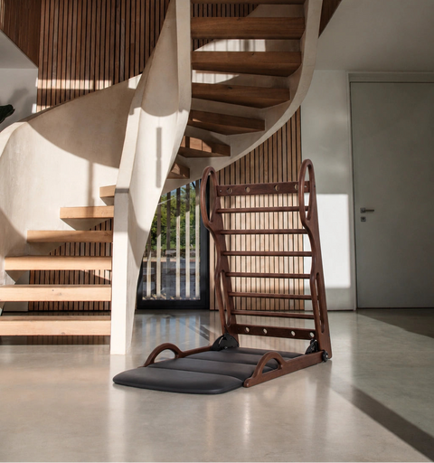 NOHRD Elasko in walnut hardwood sits on a polished concrete floor in a modern interior space with a spiral staircase and pendant lights.