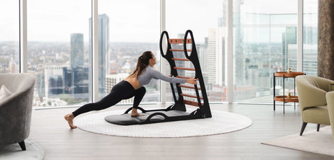 A woman in a yoga pose using a NOHRD Elasko, set in a modern living room with a city skyline view.