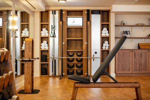 A luxury hotel gym interior featuring a wooden NOHRD Weight Bench with a black adjustable pad,and a wooden rack filled with white towels, set against warm wood paneling and floors.