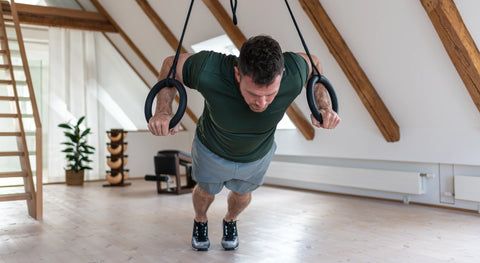 A man performing a push-up on NOHRD Sling suspended from the ceiling of a bright, modern home gym with wooden beams and light wood floors.